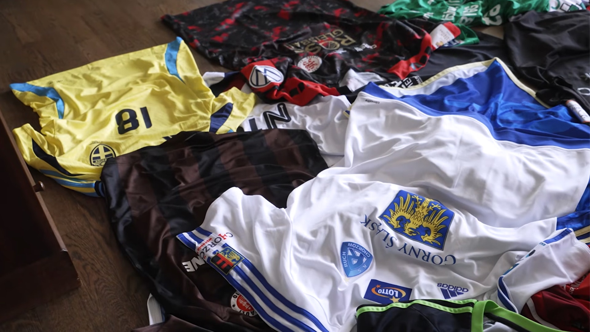 En samling fotbollströjor i olika färger utlagda på ett trägolv.
