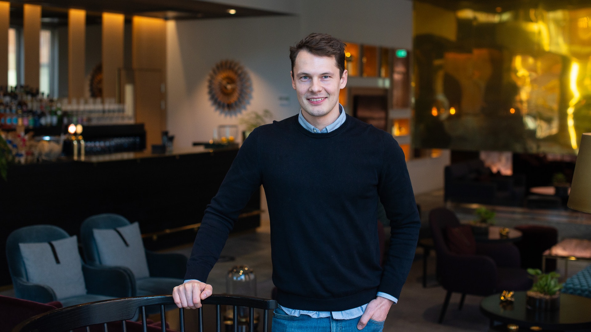 En man i mörk tröja står vid ett räcke i ett modernt interiör.