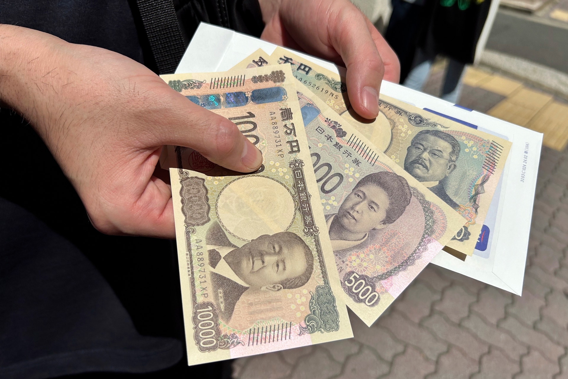 En hand håller flera japanska sedlar av olika valörer.