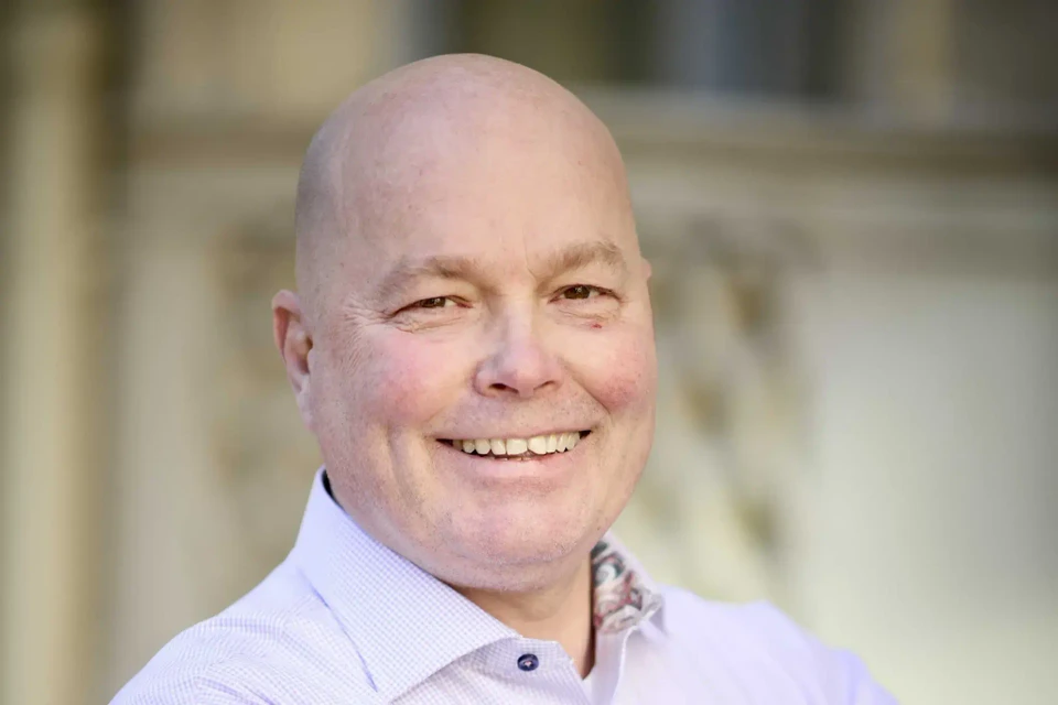 Pressbild på Ted Elvhage i ljusrosa skjorta. Han ler.