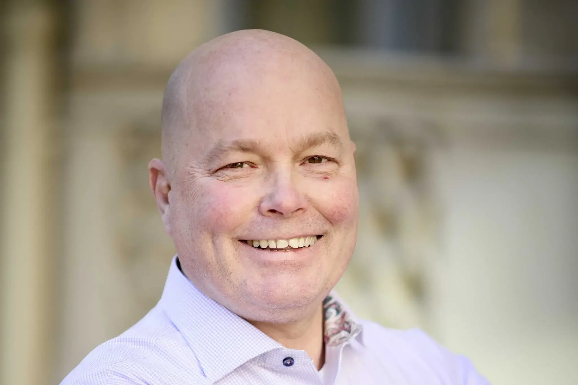 Pressbild på Ted Elvhage i ljusrosa skjorta. Han ler.