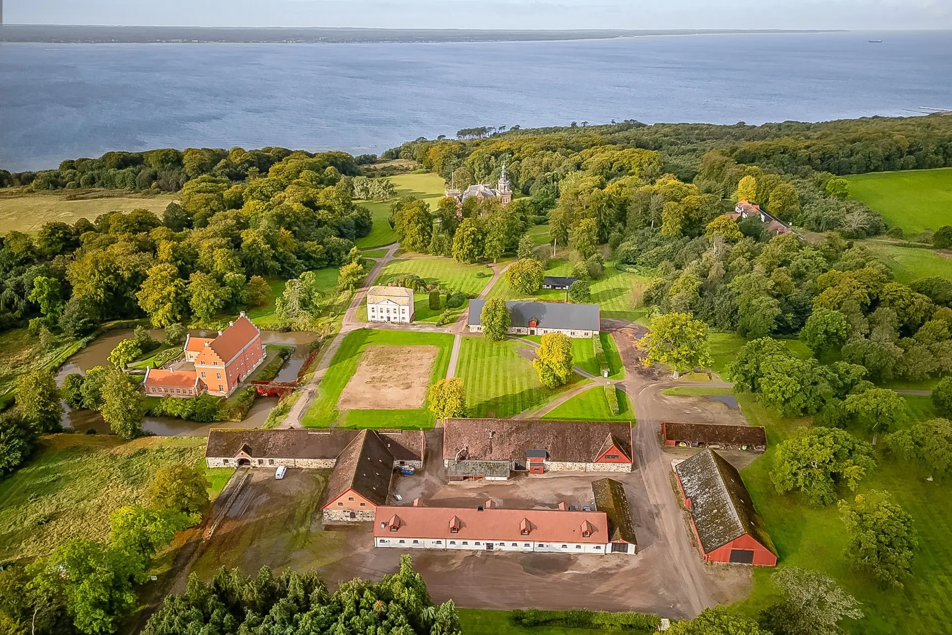 Flygfoto över en lantgård med röda och vita byggnader omgivna av gröna åkrar och träd