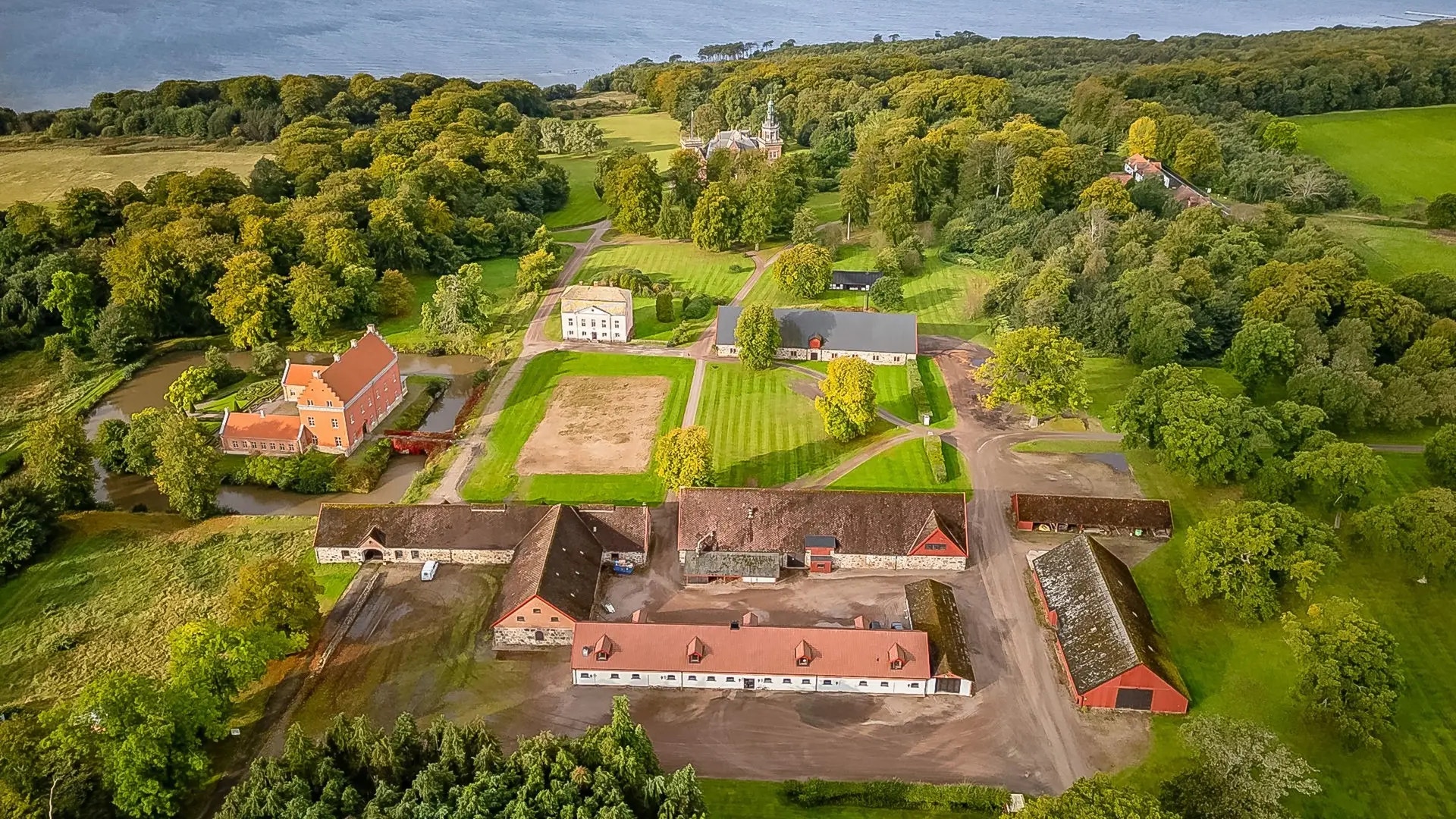 Flygfoto över en lantgård med röda och vita byggnader omgivna av gröna åkrar och träd
