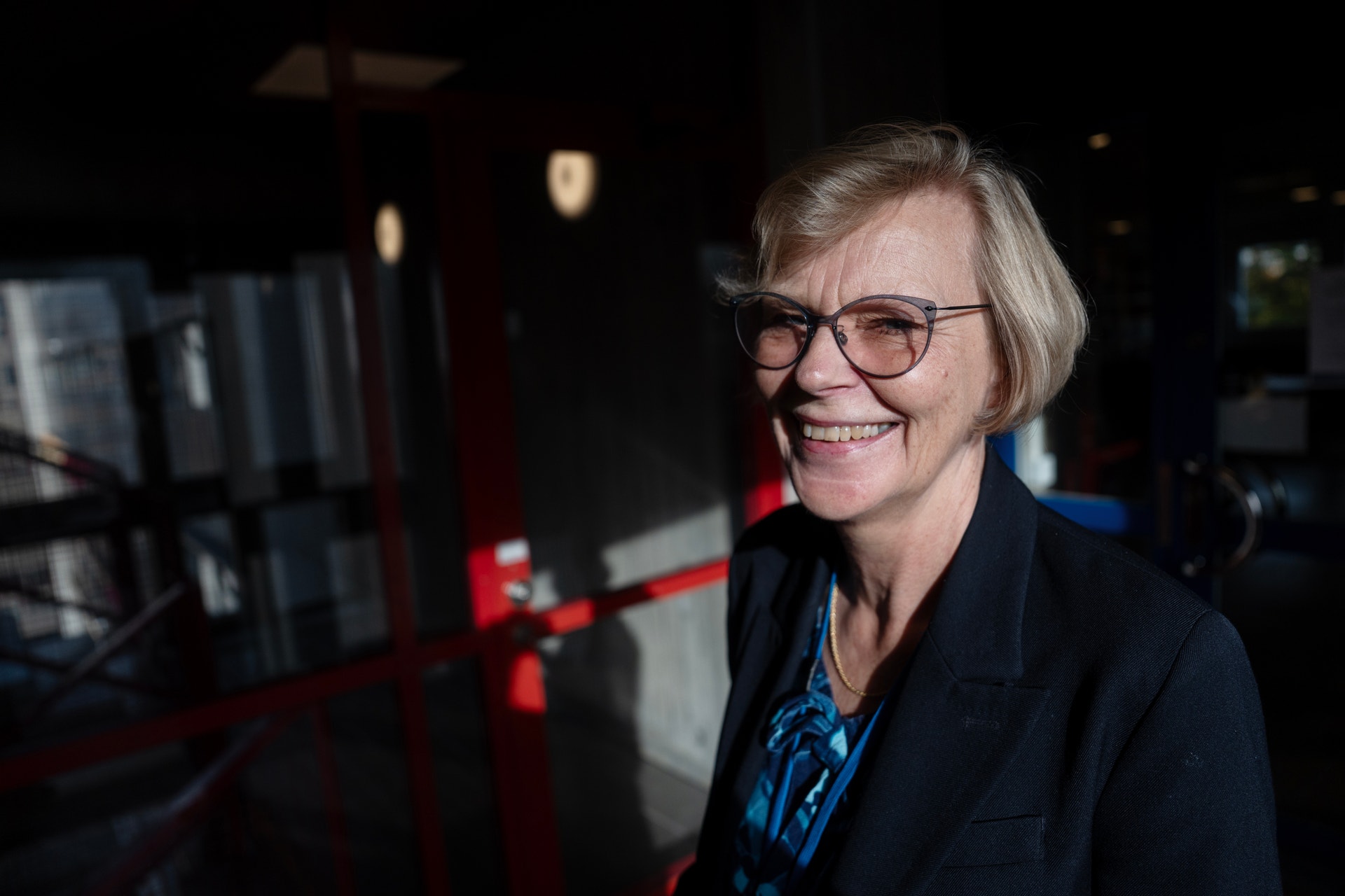 Leende kvinna med kort ljust hår och glasögon, klädd i mörk kavaj, fotograferad inomhus.