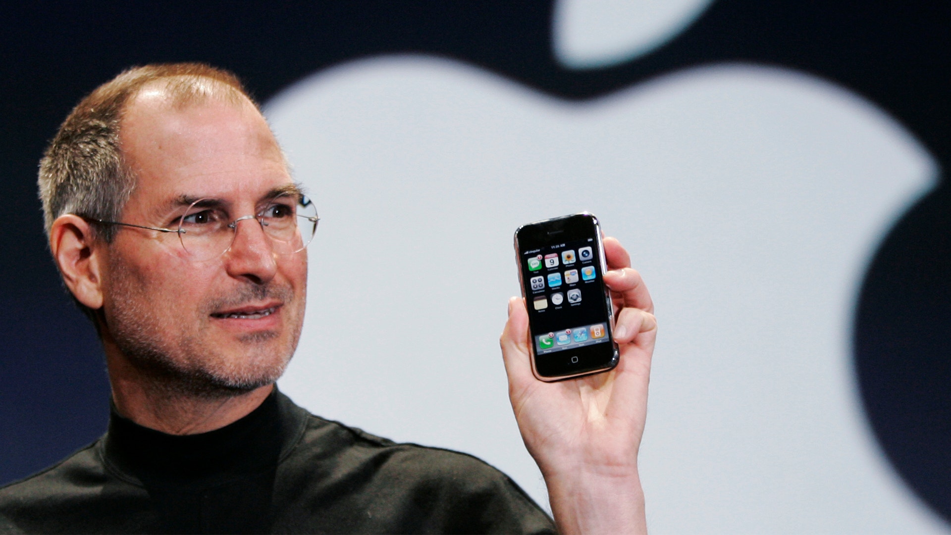 Man i svart turtleneck presenterar en iPhone framför en stor Apple-logotyp