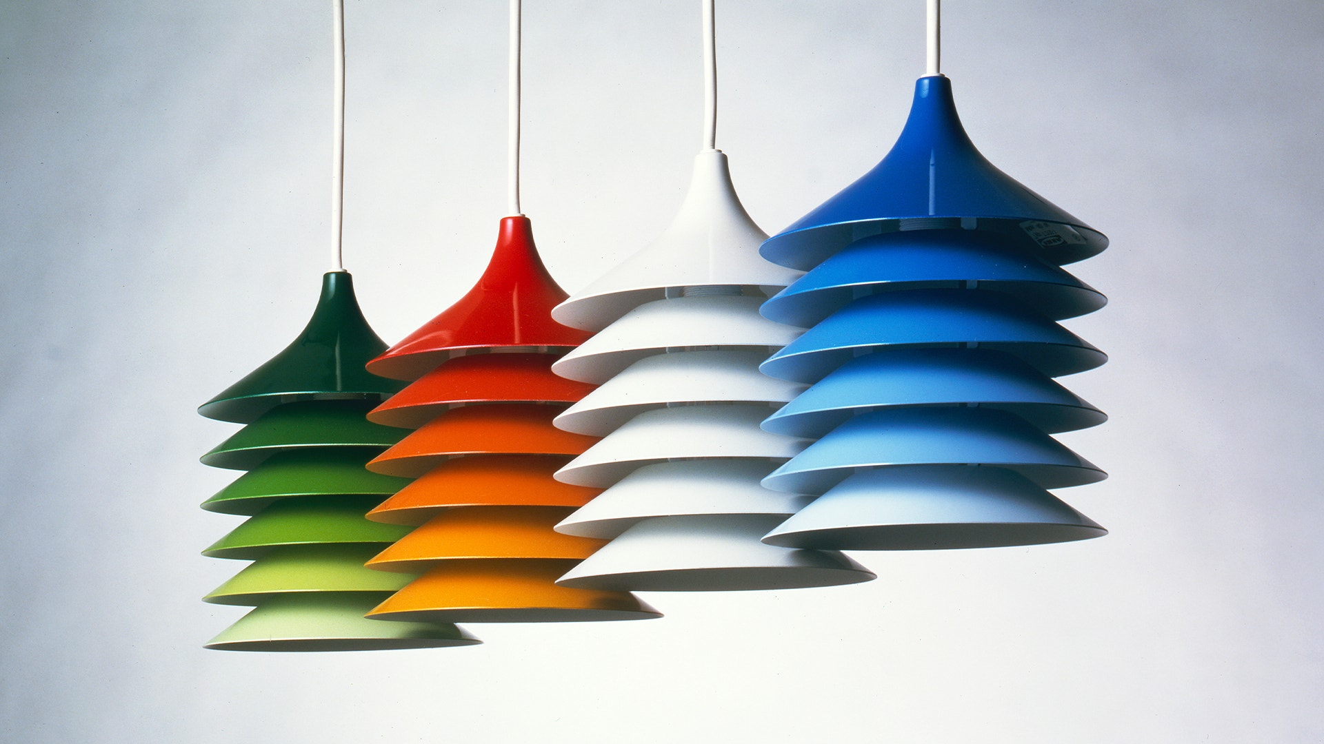 Fyra moderna hängande lampor med staplade, konformade skärmar i grönt, rött, vitt och blått