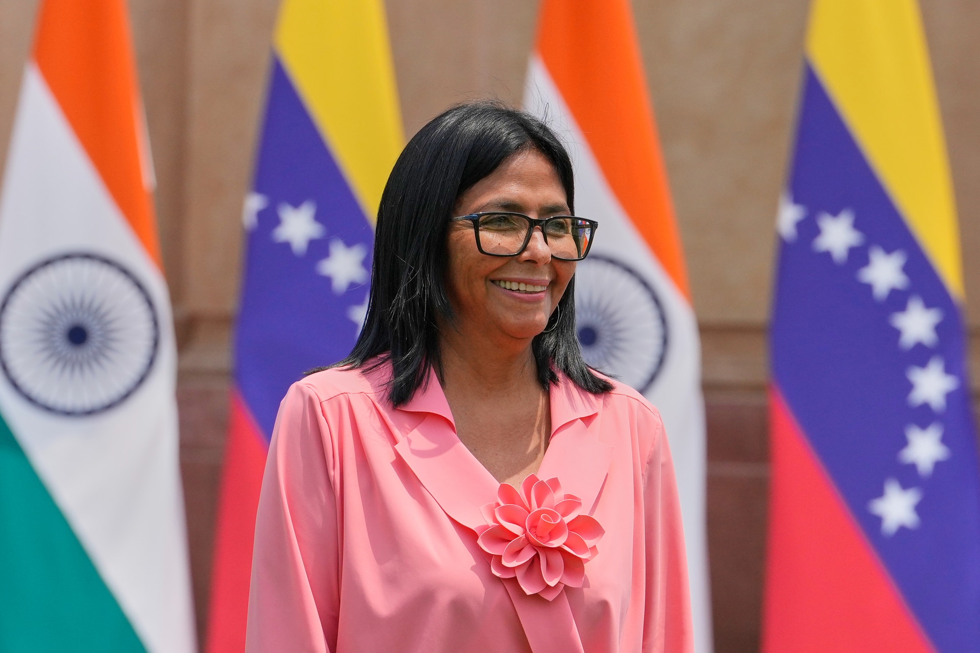 Kvinna i rosa skjorta med blomsterbrosch framför Indiens och Venezuelas flaggor.