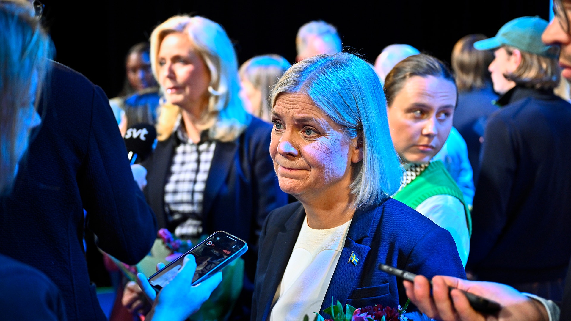En kvinna intervjuas av journalister med mikrofoner, omgiven av människor i publiken.