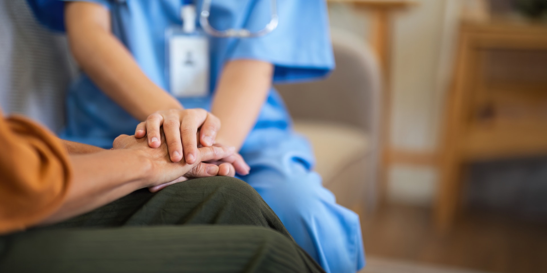 Sjukvårdspersonal i blå uniform lägger sin hand på en patients arm som ett tecken på omsorg och stöd.