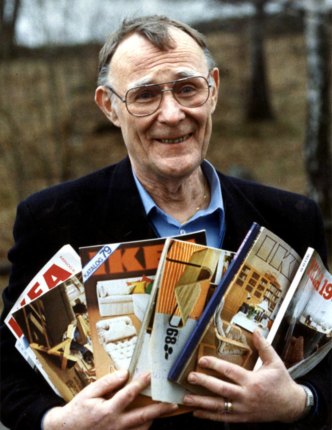 En man med glasögon håller flera IKEA-kataloger i händerna