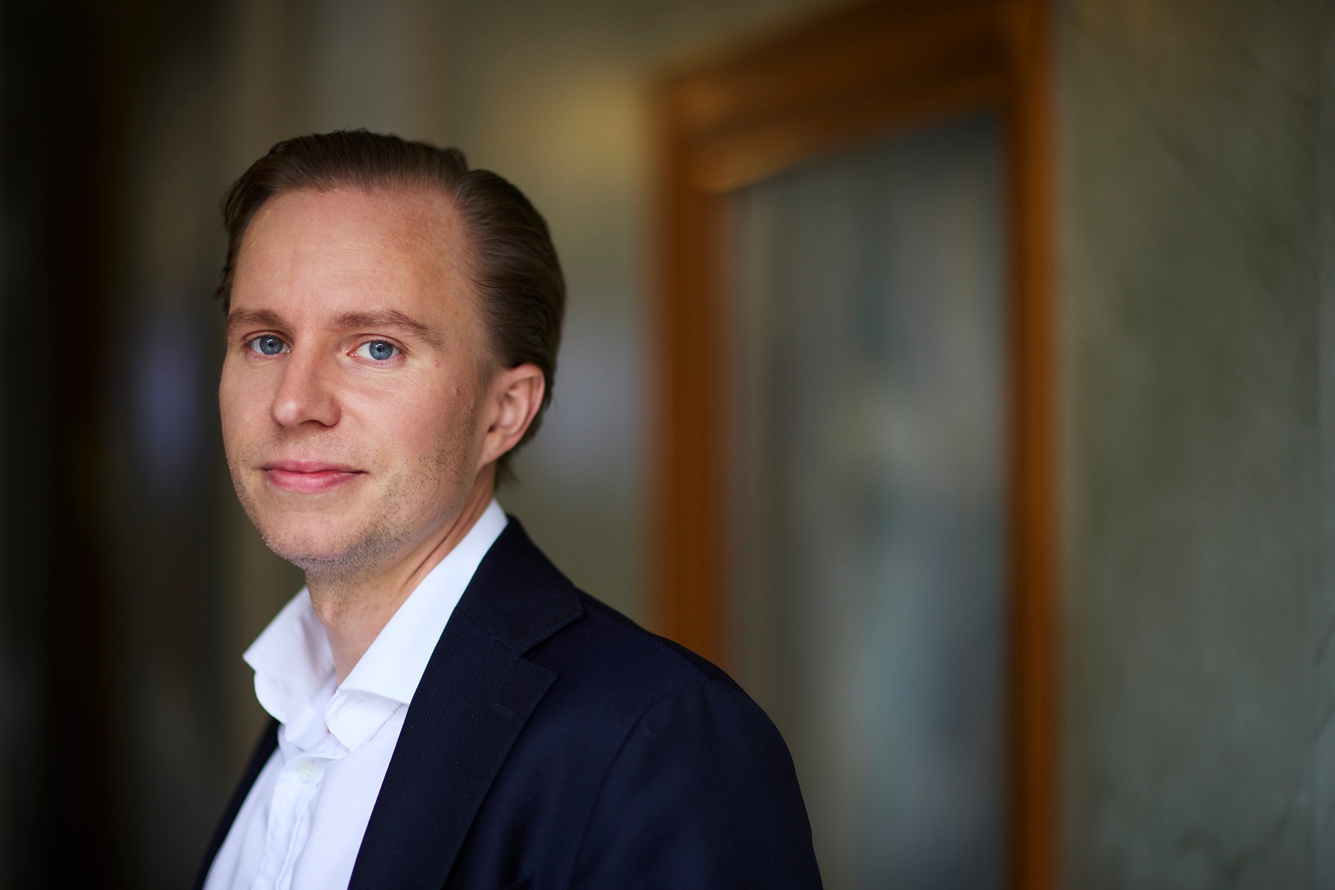 Porträtt av en man i kavaj och vit skjorta som tittar in i kameran.