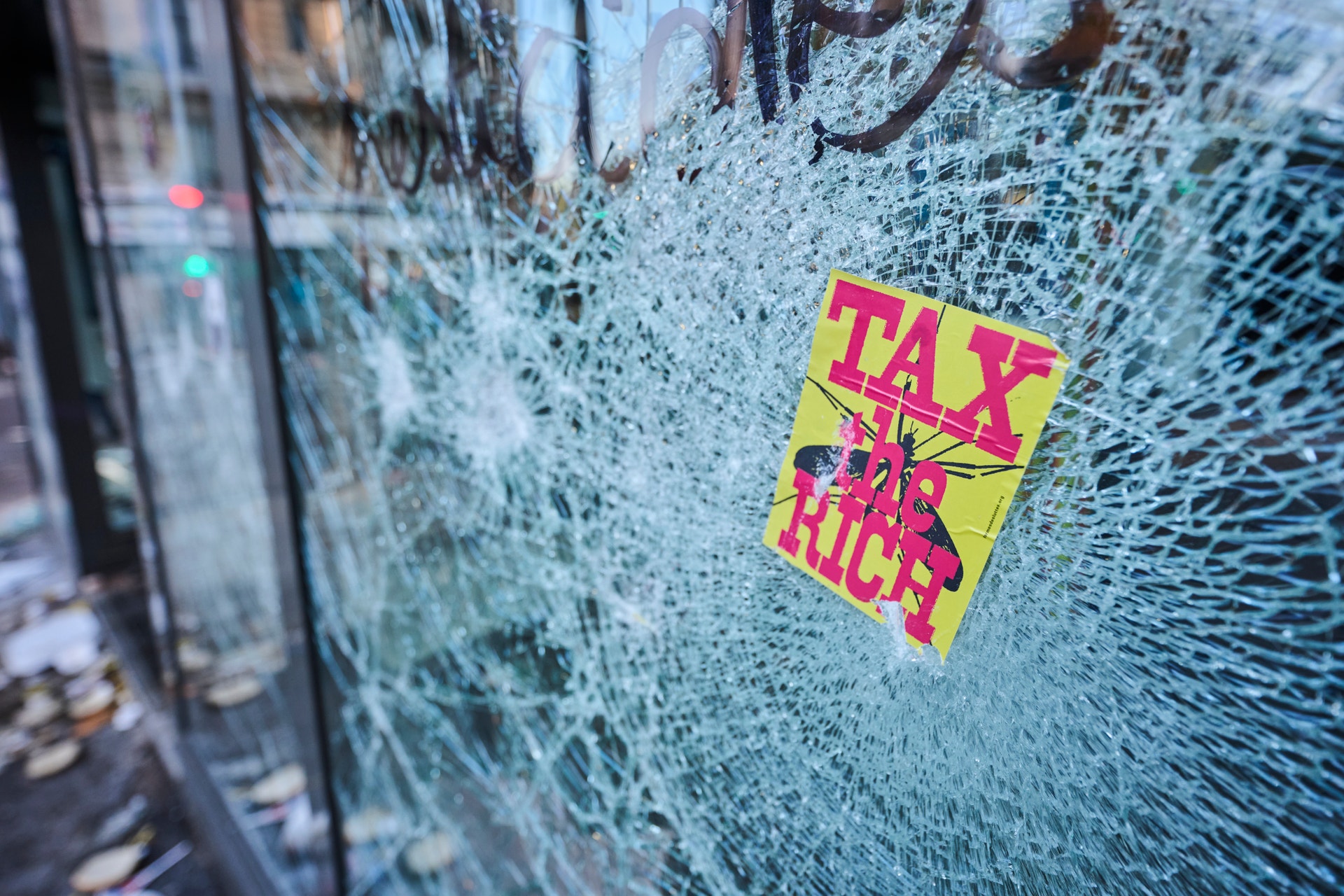 Sönderslagen skyltfönsterruta med en gul och rosa klistermärke där det står "Tax the rich".