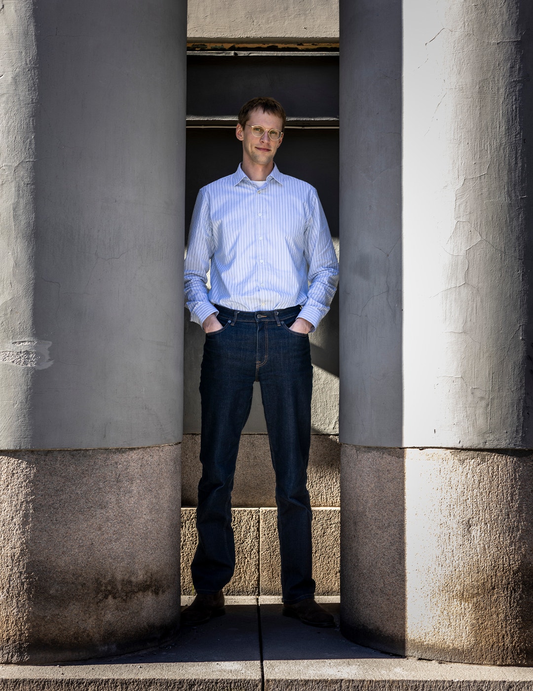 Man i blå skjorta och mörkblå jeans står mellan två stora grå kolonner.