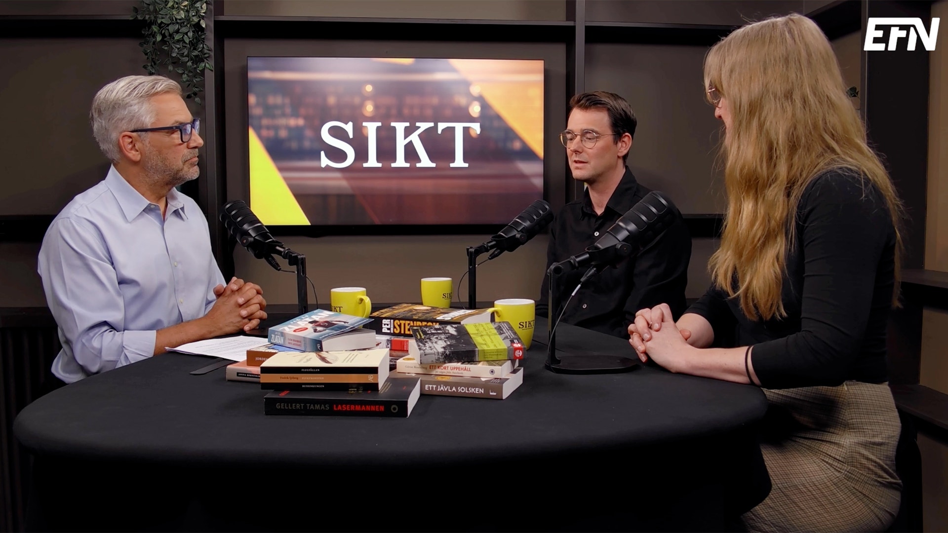 Tre personer sitter runt ett bord i en podcast-studio och diskuterar. Framför dem ligger böcker och kopp. En skärm i bakgrunden visar texten SIKT.