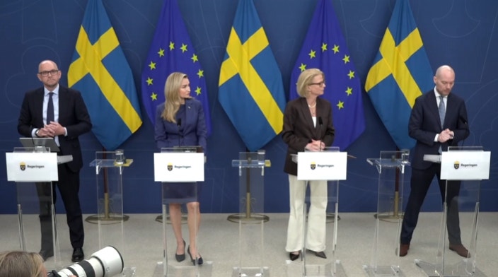 Fyra personer står vid podier under en presskonferens. I bakgrunden syns svenska flaggor och EU-flaggor.