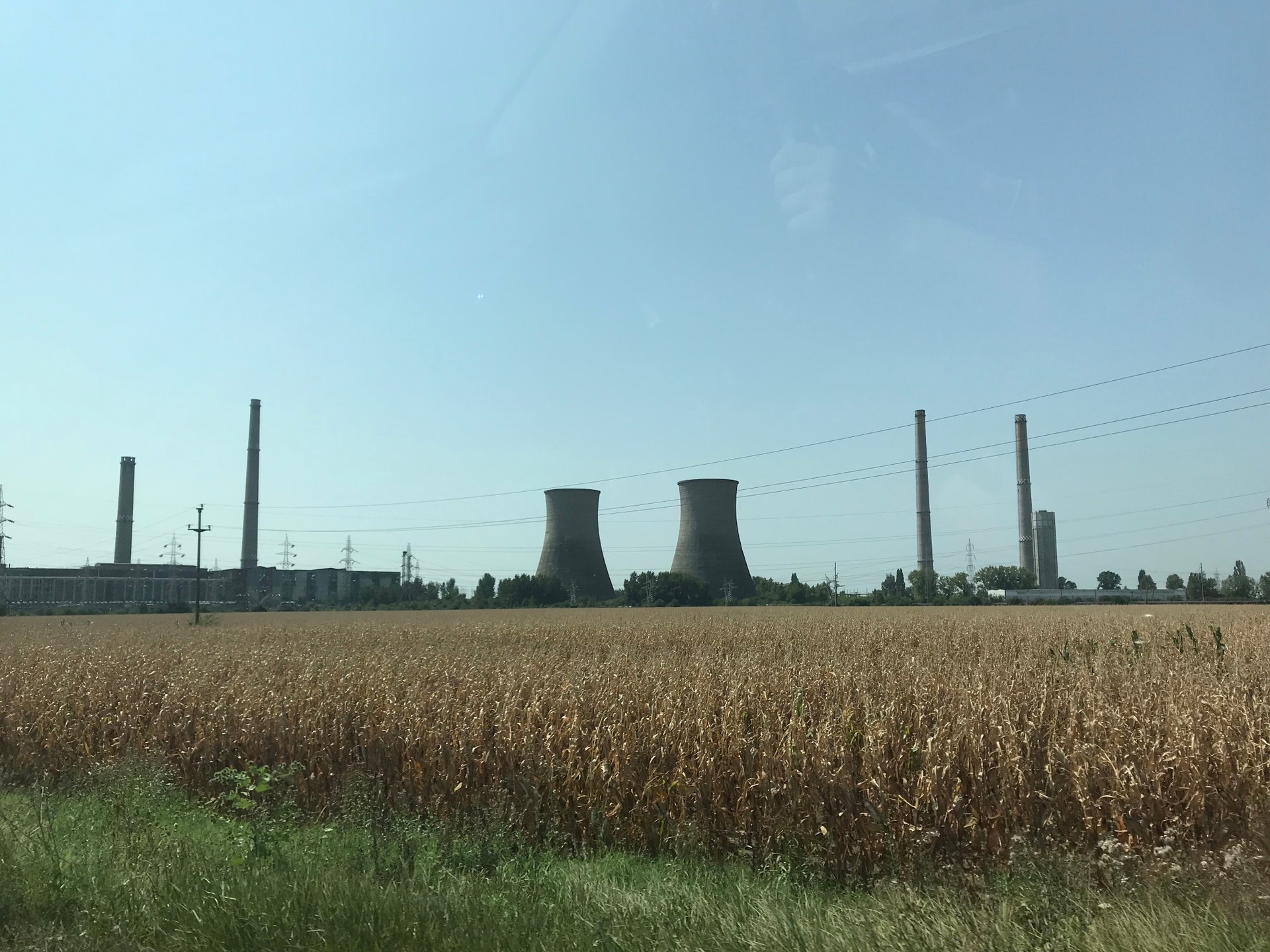 Industrianläggning med stora kyltorn i bakgrunden bakom ett kornfält under blå himmel.