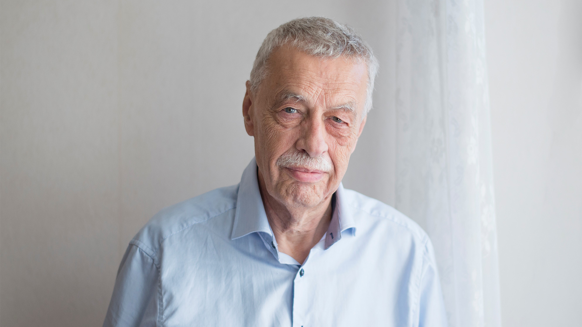 Porträtt av en äldre man med grått hår, iklädd ljusblå skjorta