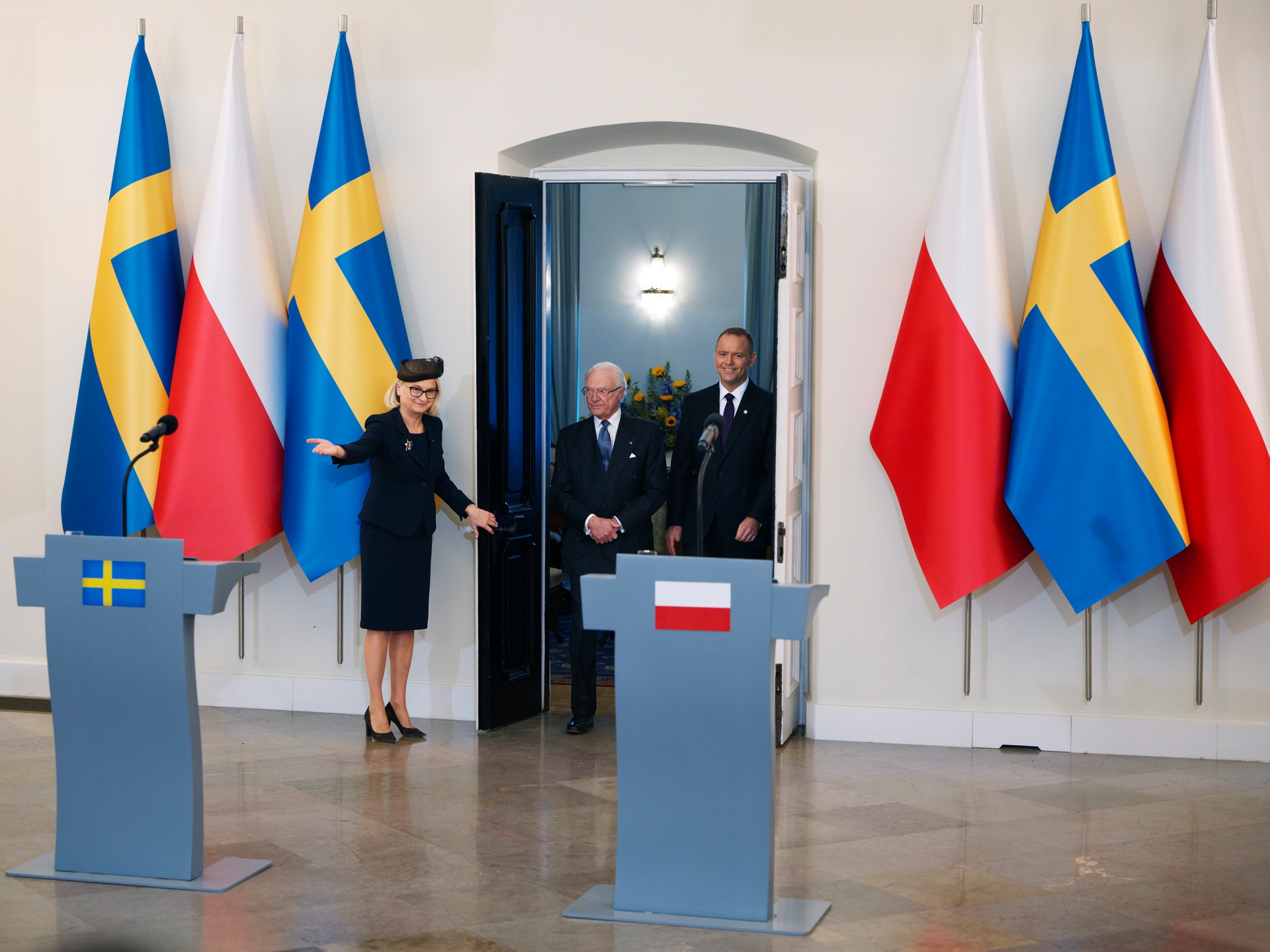 Formell möte mellan svenska och polska officiella representanter i en sal med svenska och polska flaggor.