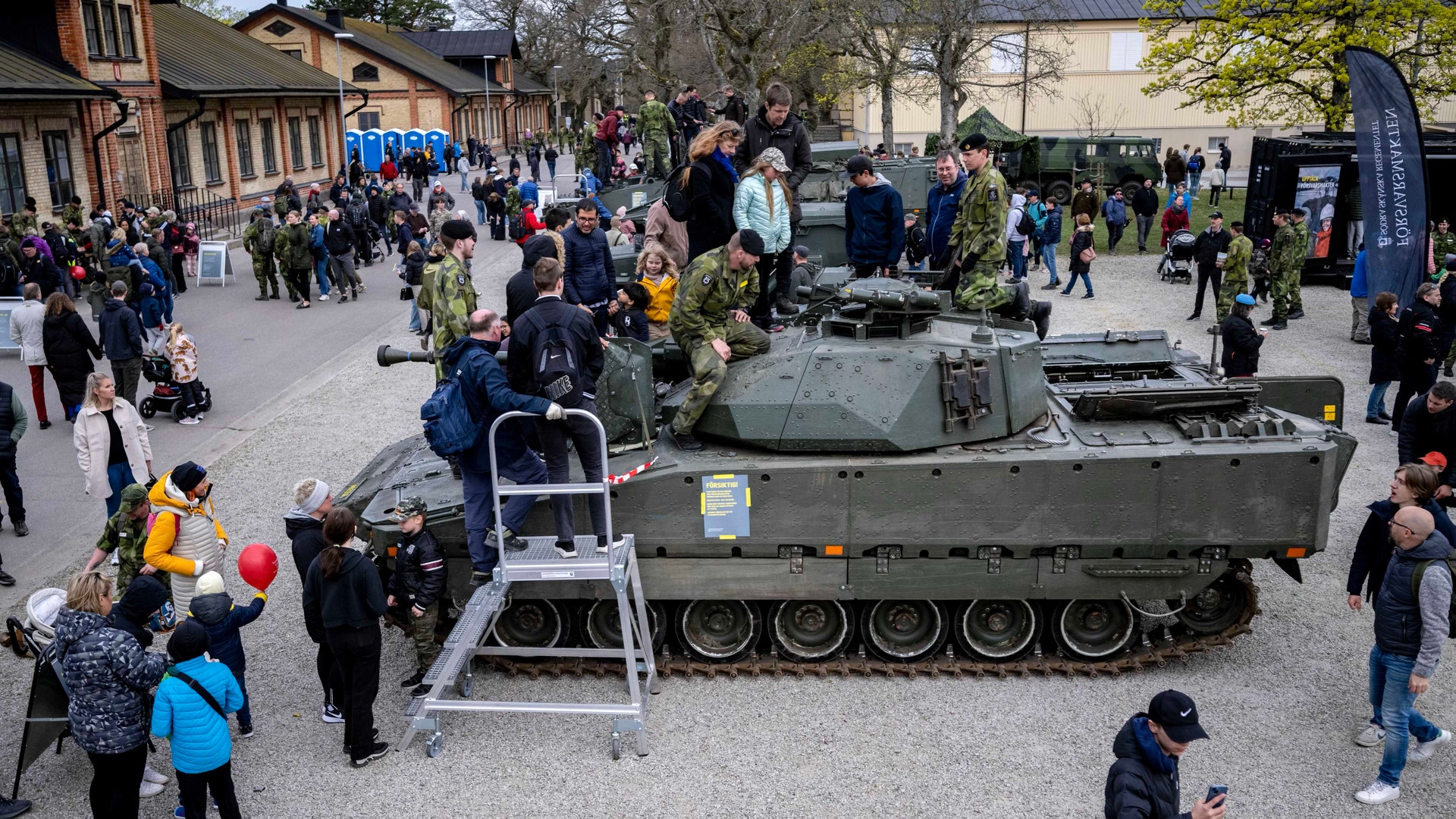 En militär stridsvagn utställd på en öppen plats med många människor som står omkring och tittar på den.