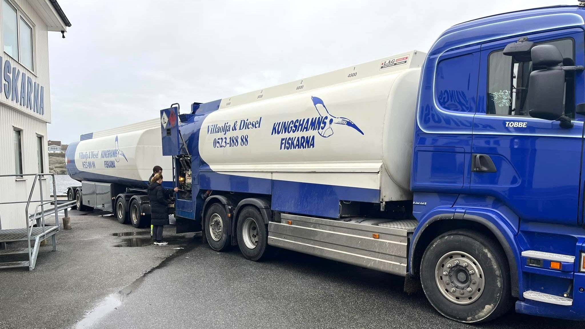 En blå och vit tankbil från Kungshamnsfiskarna parkerad vid en hamnanläggning