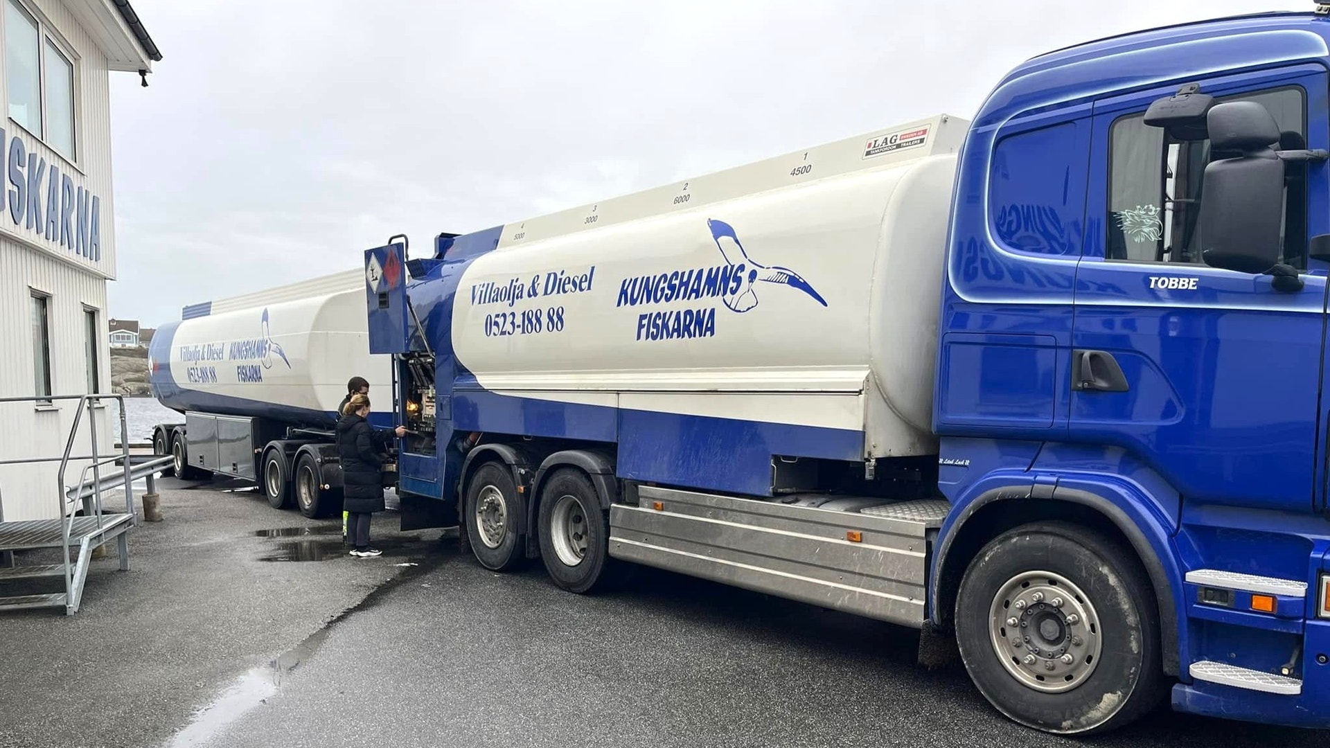 En blå och vit tankbil från Kungshamnsfiskarna parkerad vid en hamnanläggning