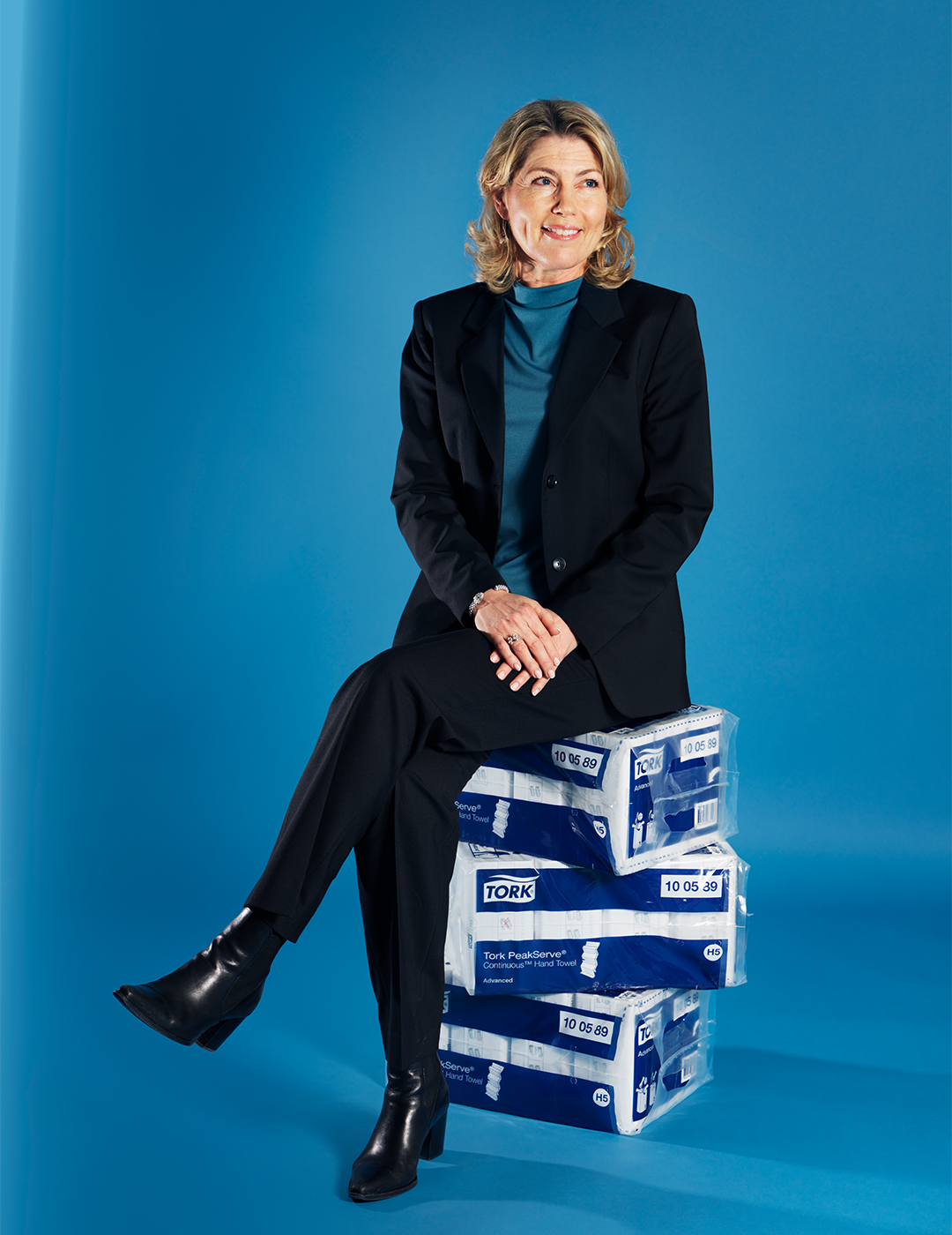 Professionell kvinna i svart kostym sitter på staplade produktlådor mot blå bakgrund