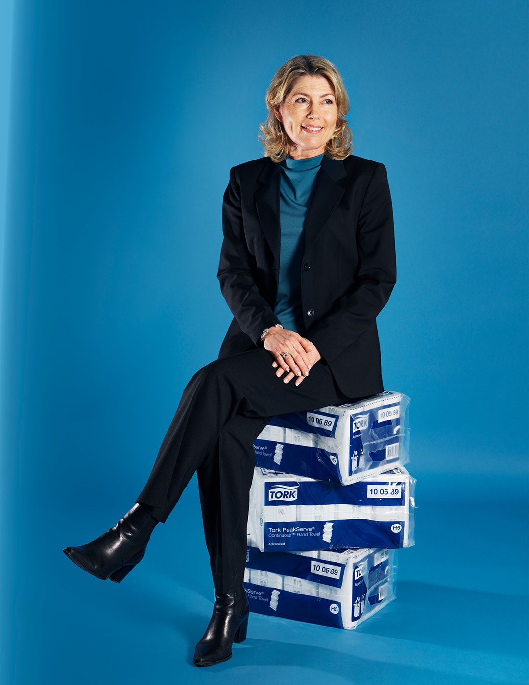 Professionell kvinna i svart kostym sitter på staplade produktlådor mot blå bakgrund