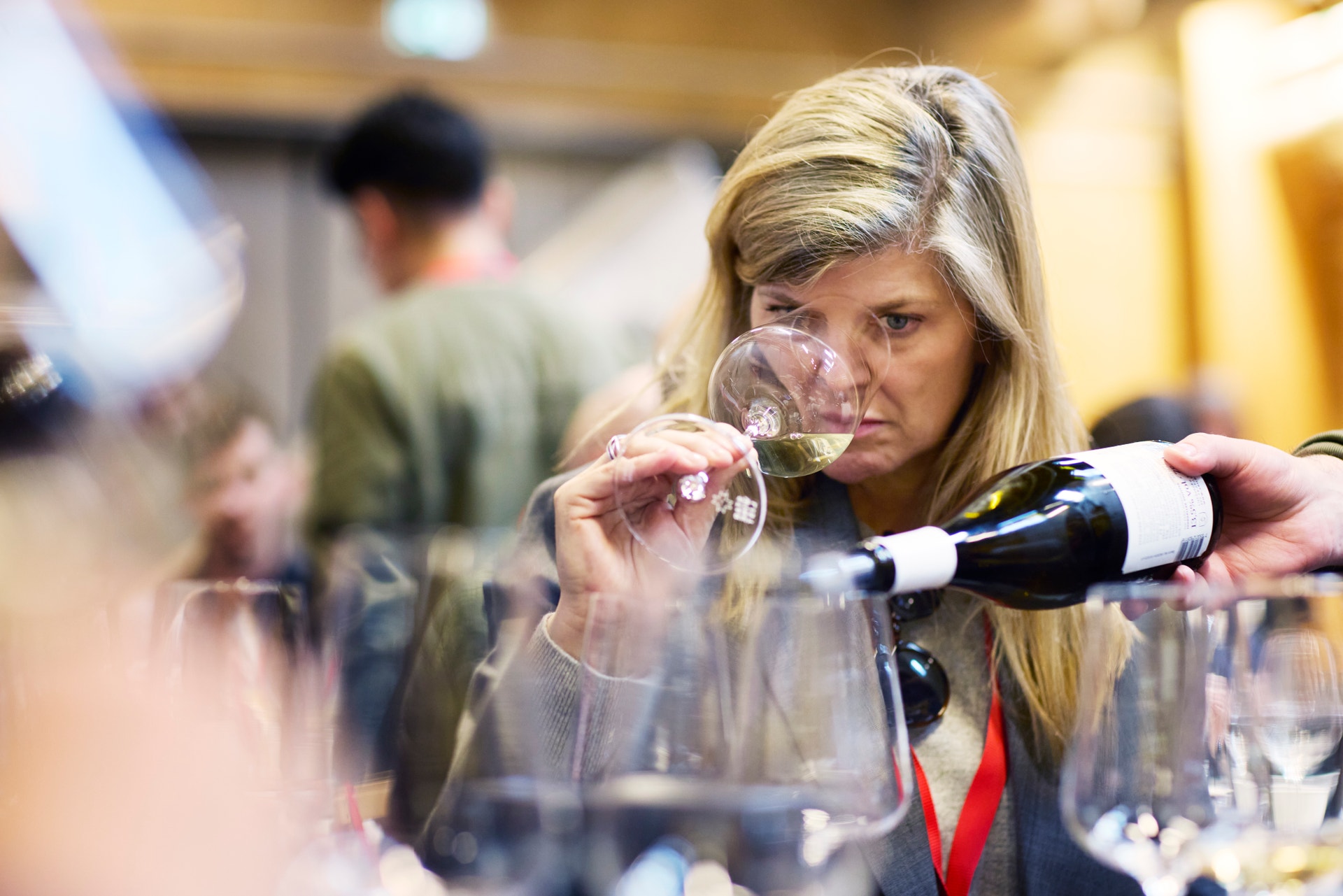 Kvinna häller vin från en flaska in i ett vinglas under en vinevent.