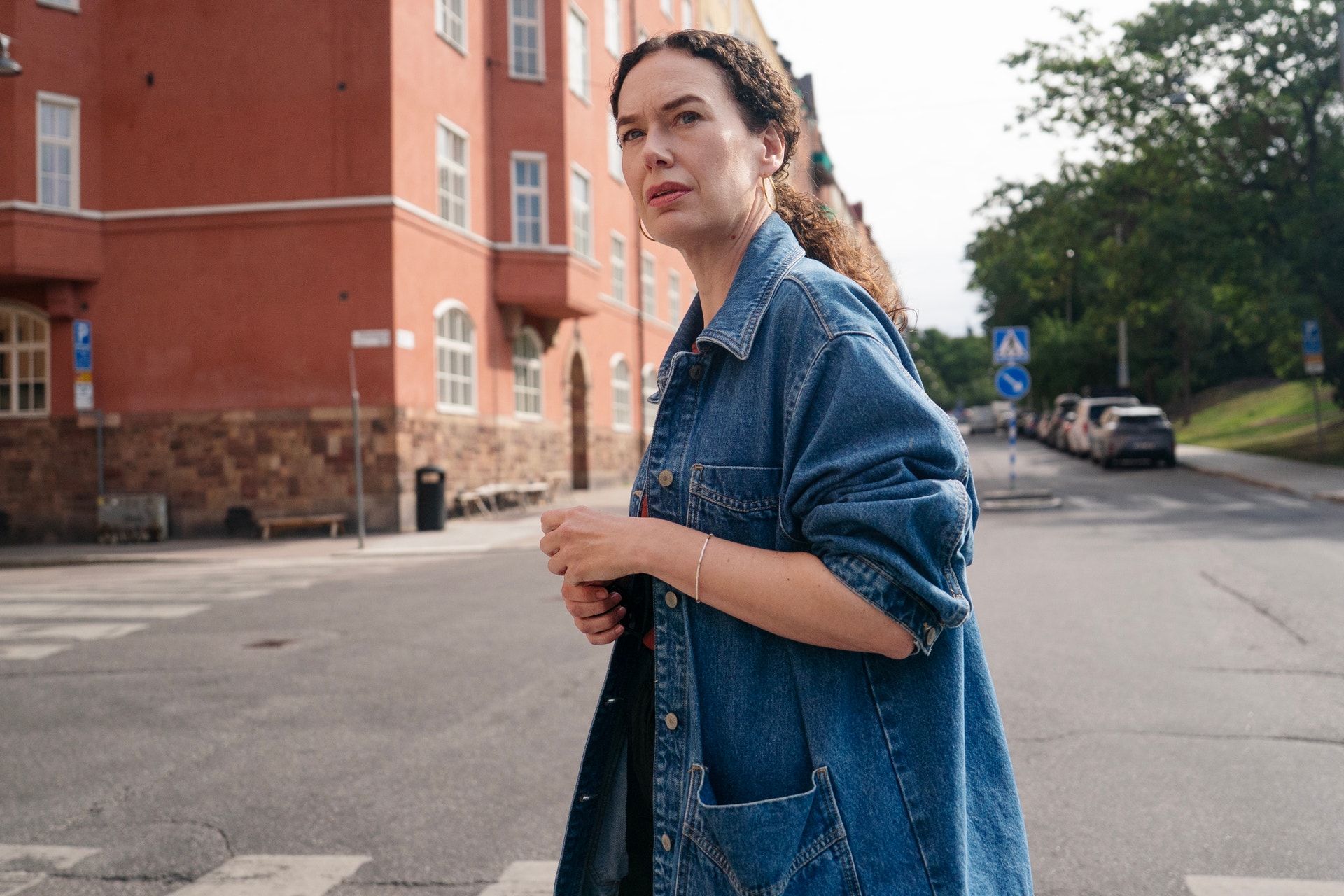 Person i blå jeansskjorta står framför en röd tegelbyggnad och tittar över axeln mot kameran.