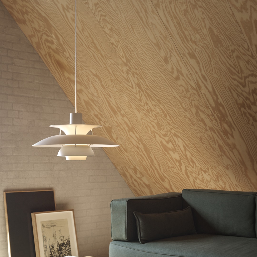 Modernt vardagsrum med hängande vit designlampa, träväggpanel och grön soffa med svarta kuddar.