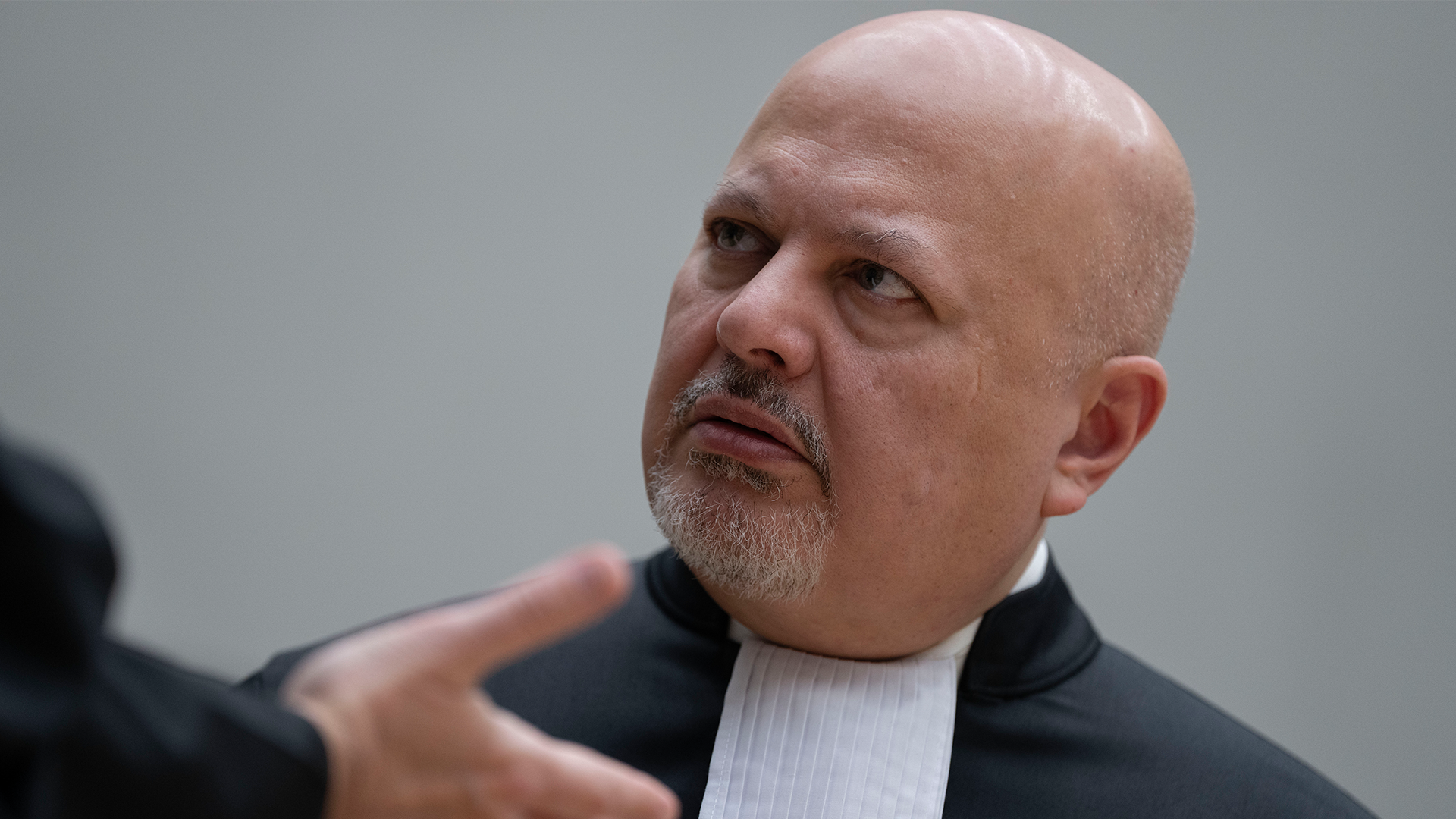 Karim Khan i domstol med svart kopa. Han ser förbryllad ut.