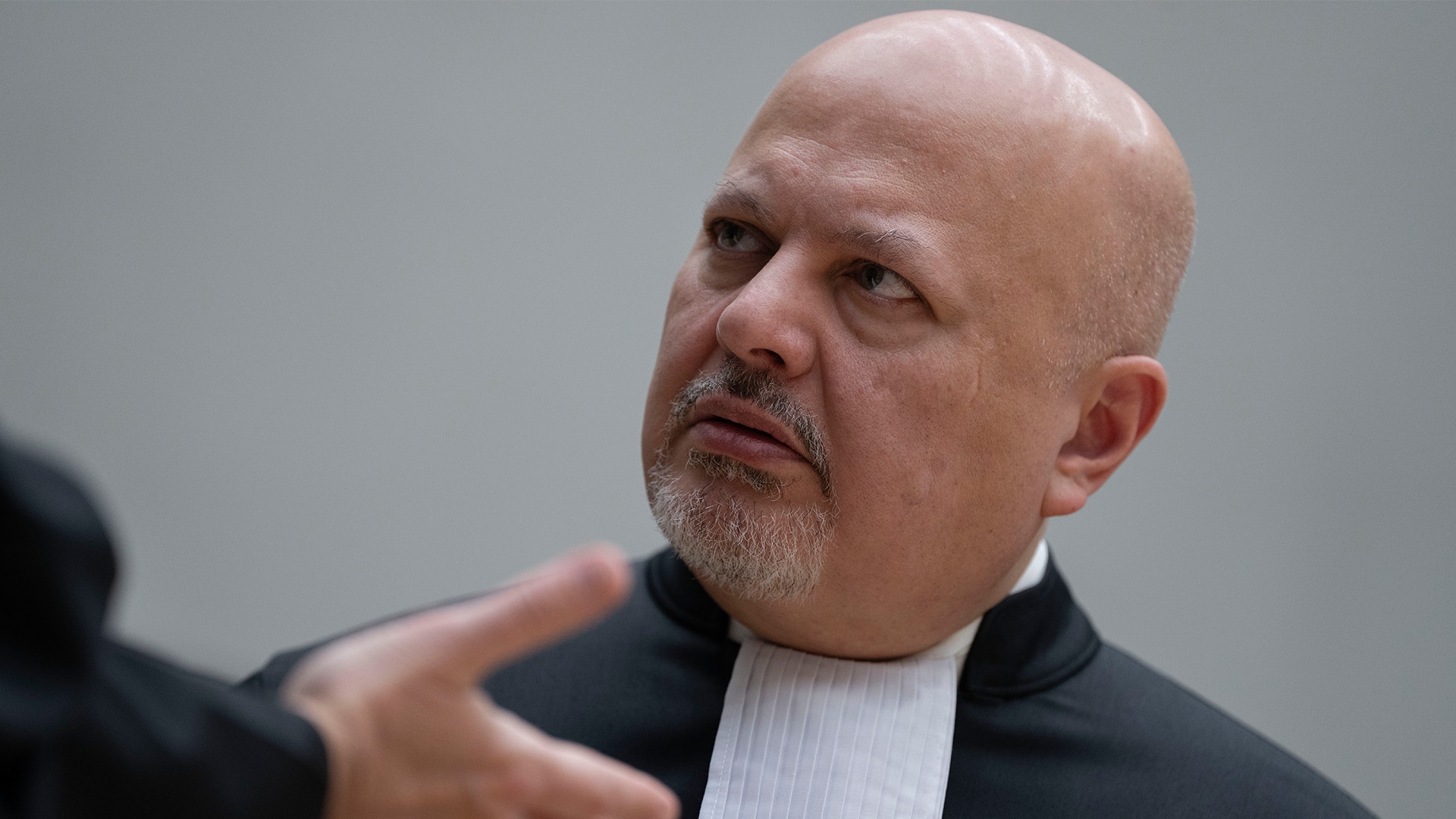 Karim Khan i domstol med svart kopa. Han ser förbryllad ut.