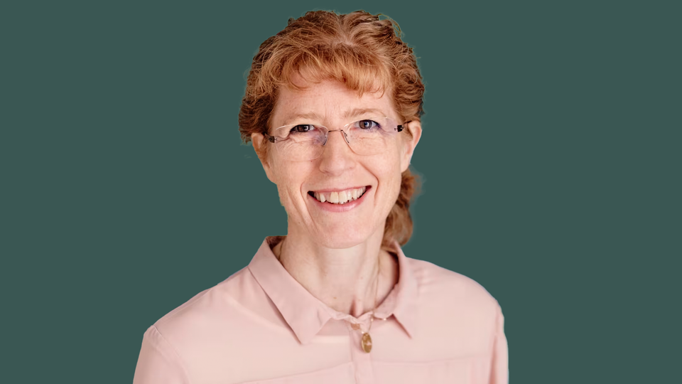 Porträttfoto av en leende kvinna med rött hår mot grön bakgrund