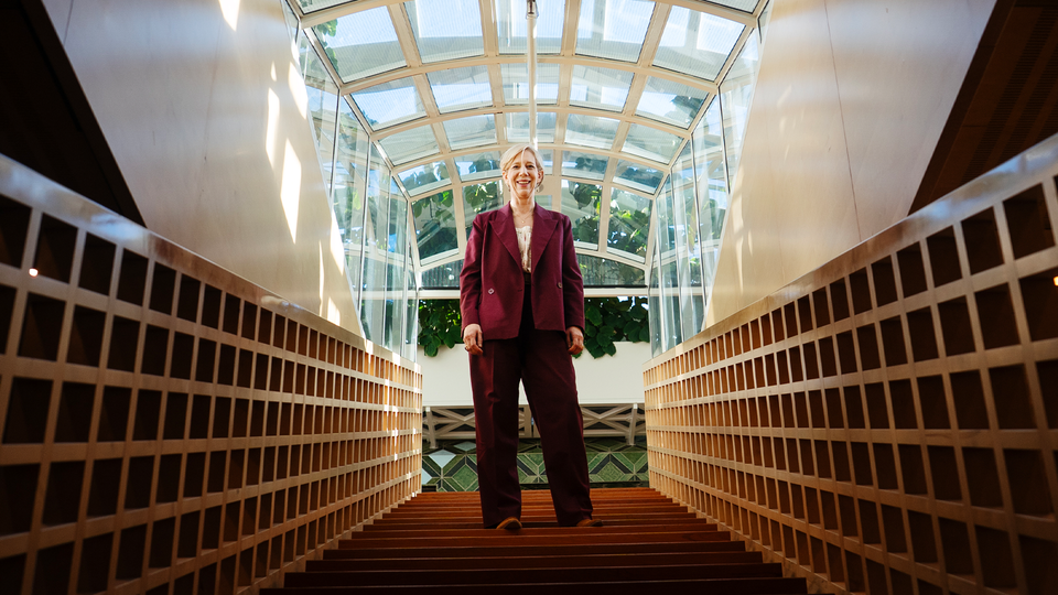 Anna Breman står i en trappa på Riksbanken. Genom fönstret i taken sipprar solen in. 