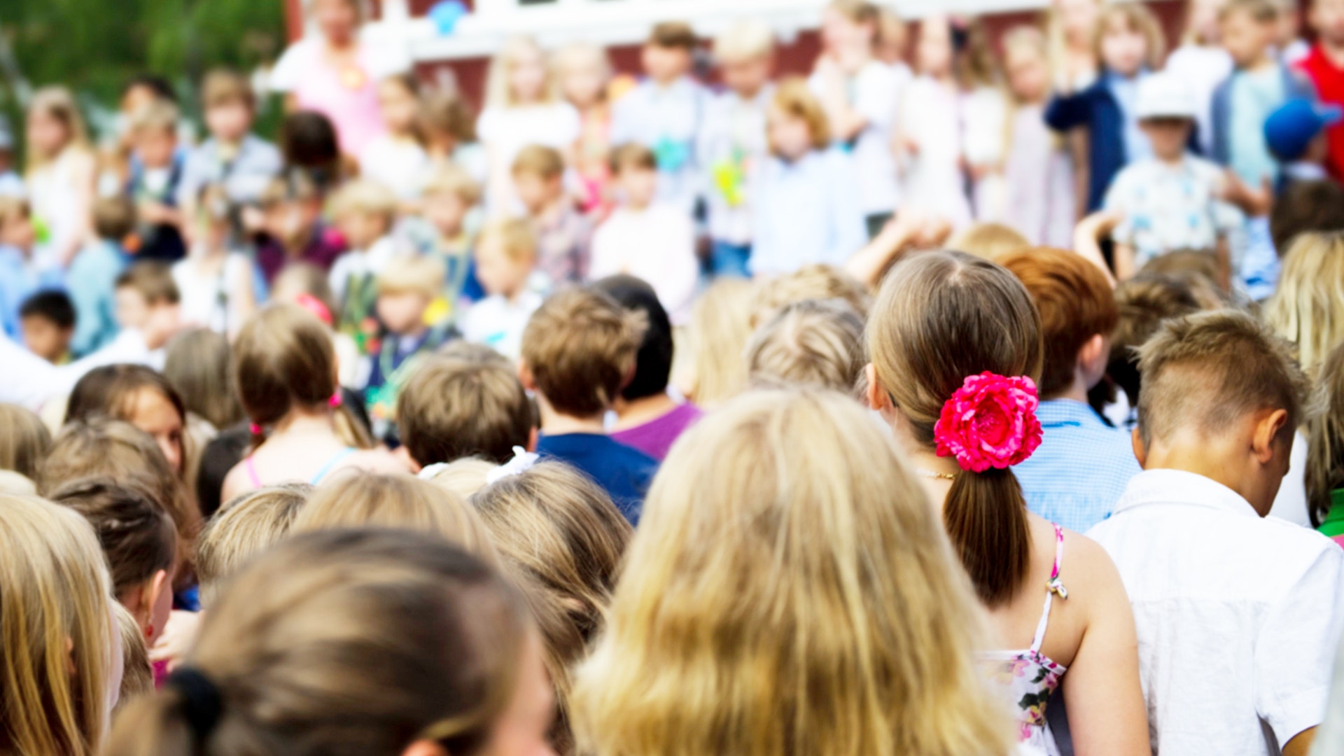 En skolavslutning på ett mellanstadie i jui. På bilden ser man ryggar av en drös uppklädda barn som längtar till sommarlov.