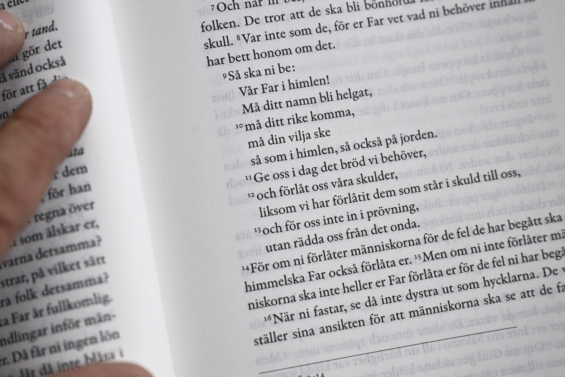 En hand håller i en uppslagen bok med bibeltext.