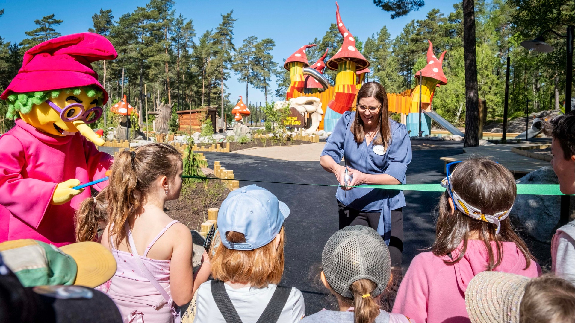 Invigning av Trollskogen med barn och personal som möter färgglada karaktärmaskoter i en parkmiljö.