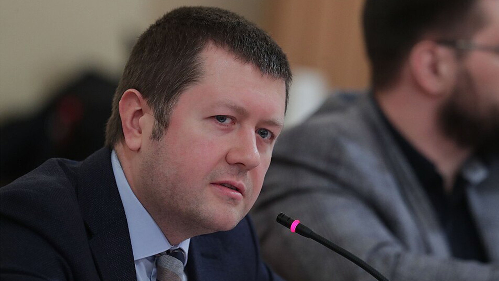 Man i kostym talar vid en mikrofon under ett möte.