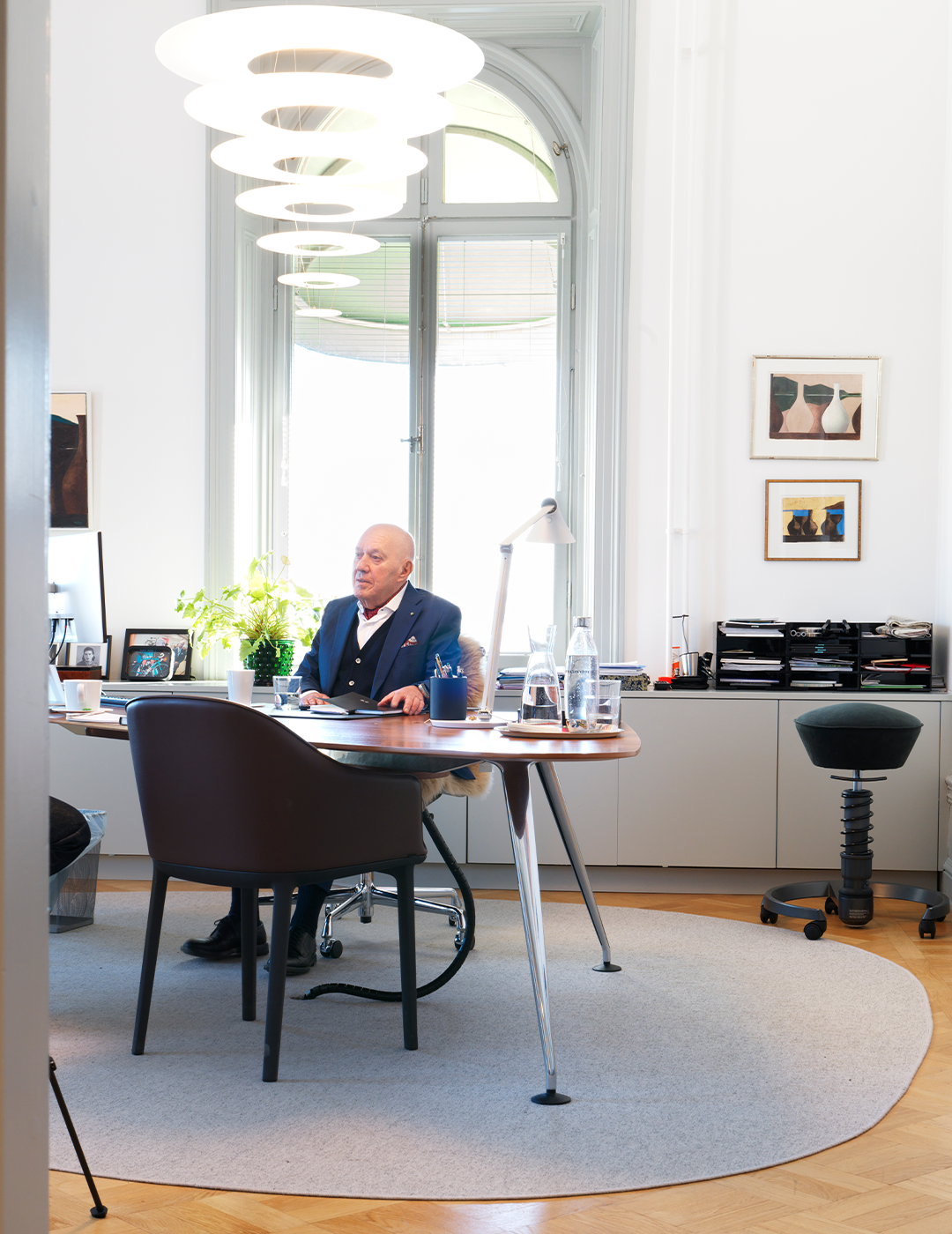 Man sitter vid sitt skrivbord i ett modernt kontor med stora fönster och stilren inredning.