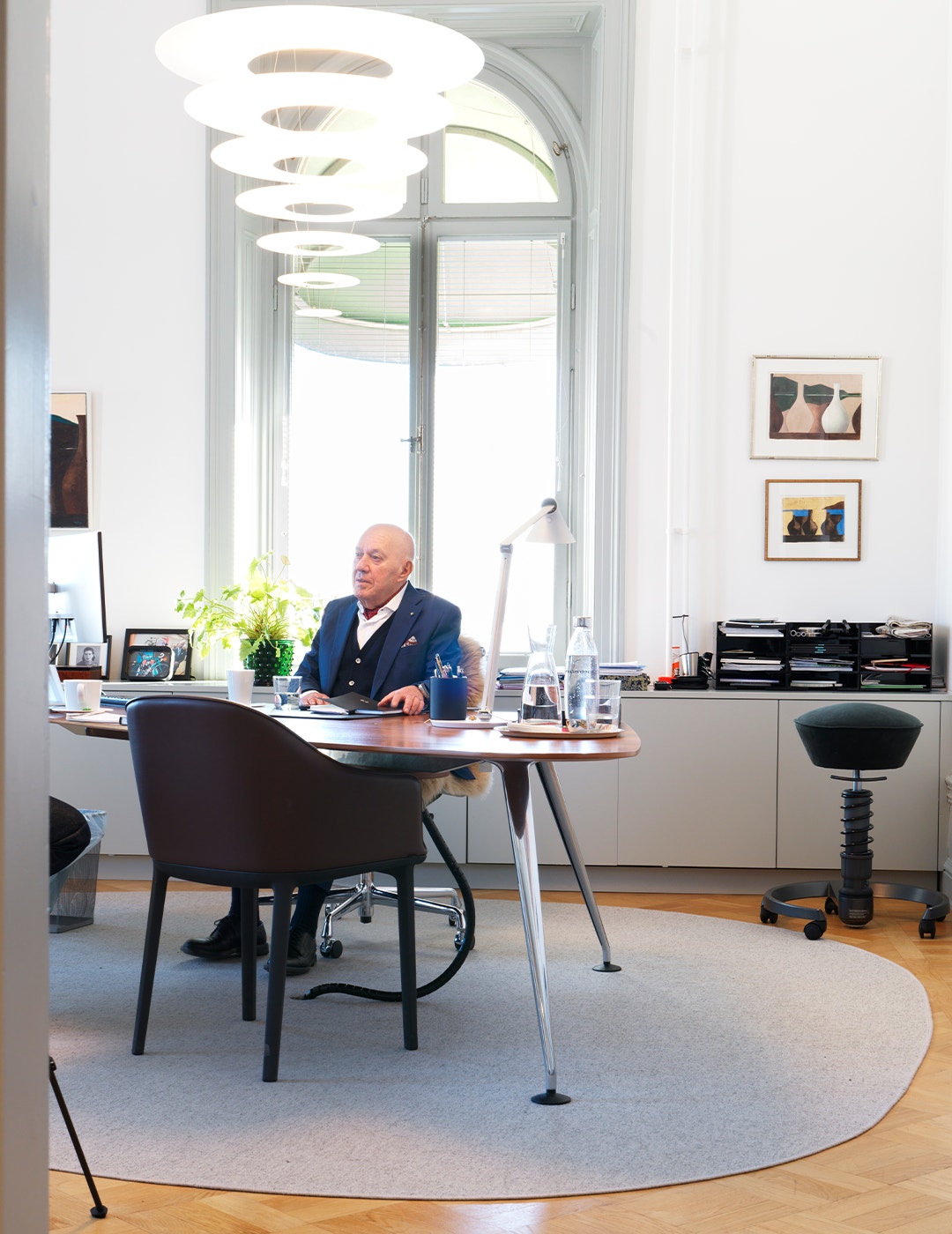 Man sitter vid sitt skrivbord i ett modernt kontor med stora fönster och stilren inredning.