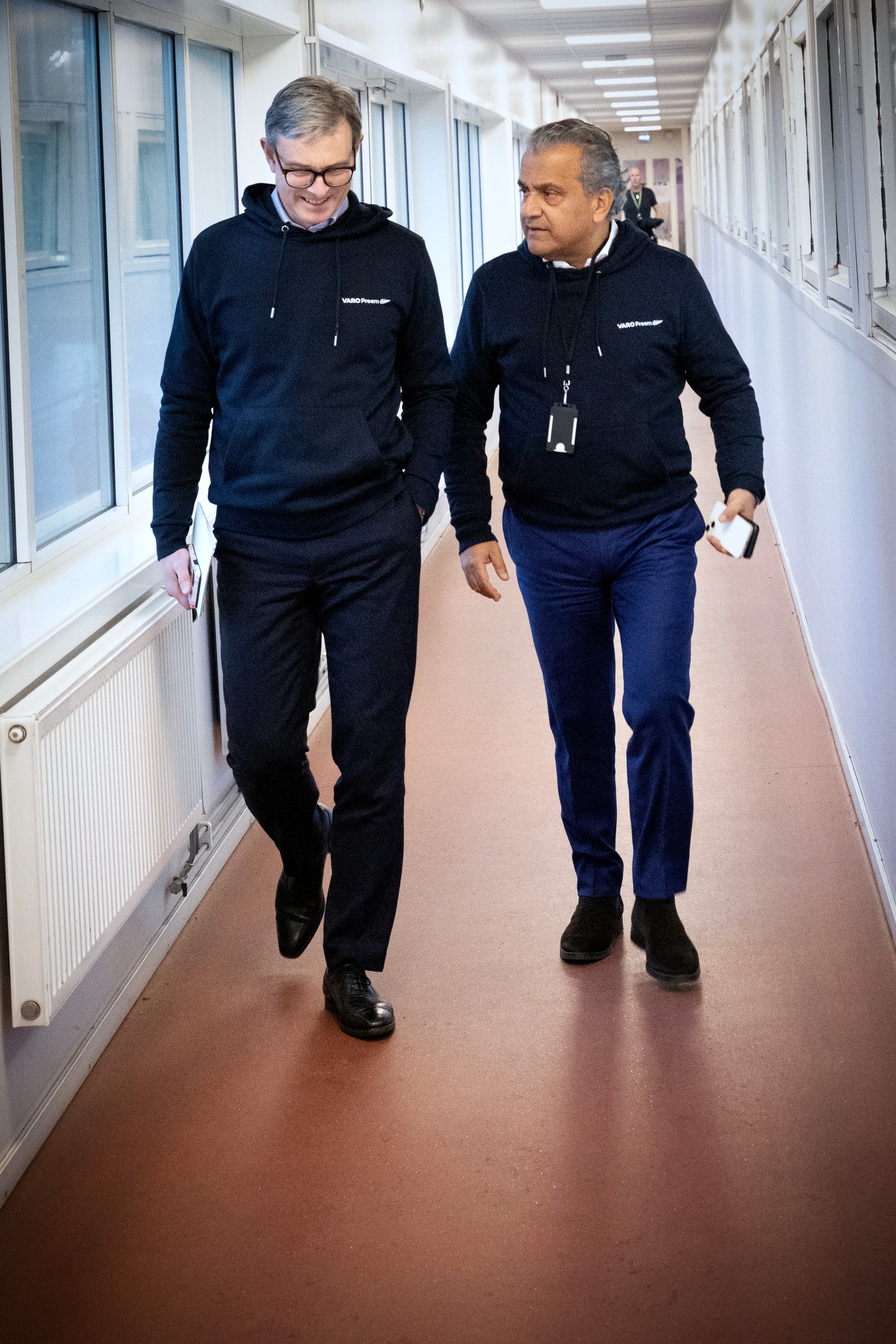 Två män går tillsammans i en vit korridor. Båda är klädda i mörkblå hoodies.