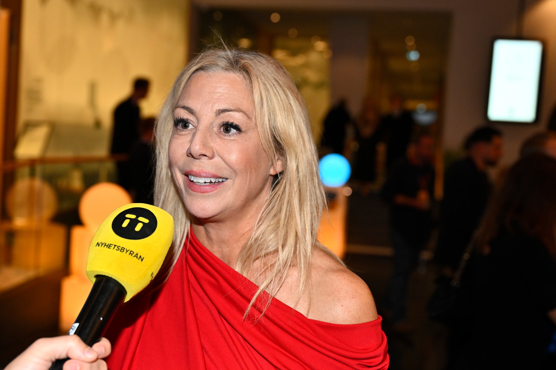 En leende kvinna i röd klänning intervjuas med en mikrofon från Nyhetsbyrån TT.