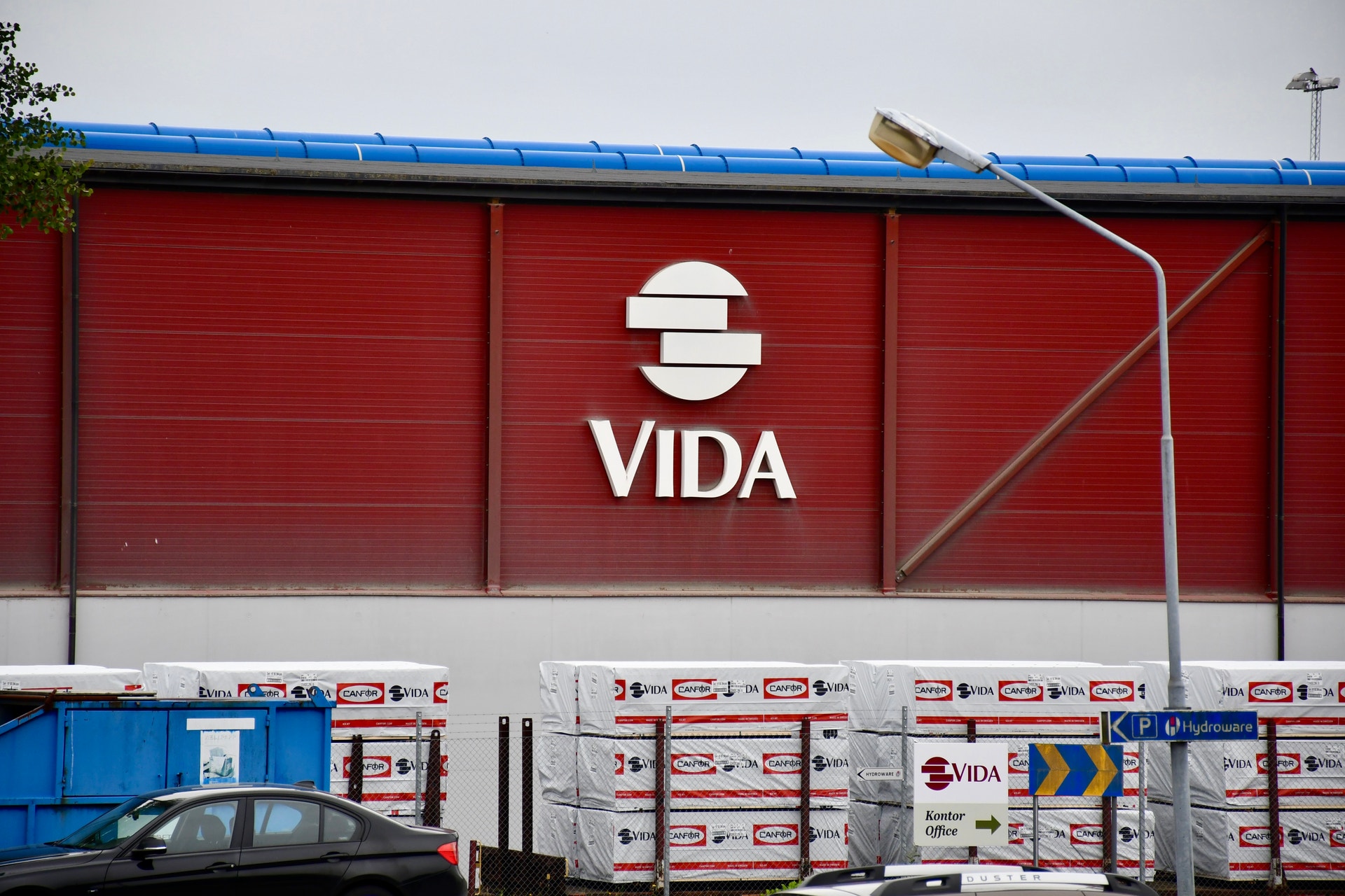 Röd industribyggnad med Vidas logotyp på fasaden. Framför byggnaden syns travar med packat virke.