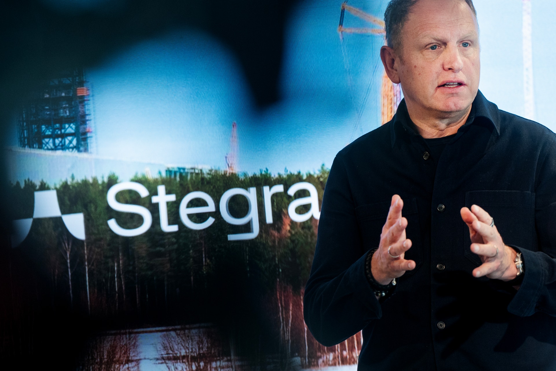 Man i svart skjorta presenterar framför Stegra-logotyp och industriell bakgrund.