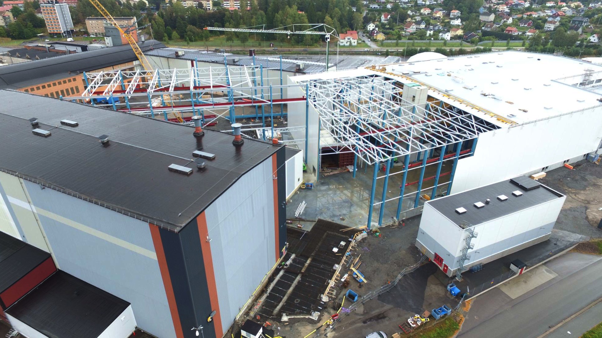 Flygbild över en industribyggnad under uppbyggnad, med stålkonstruktioner och kranar synliga.