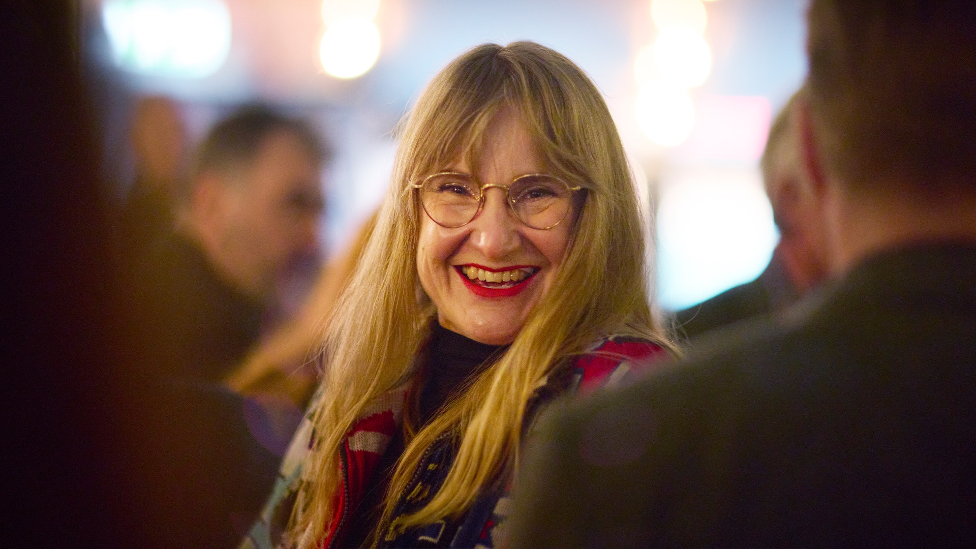 Porträtt av Sara Martinsson, en kvinna med långt blont hår och glasögon som ler mot kameran.