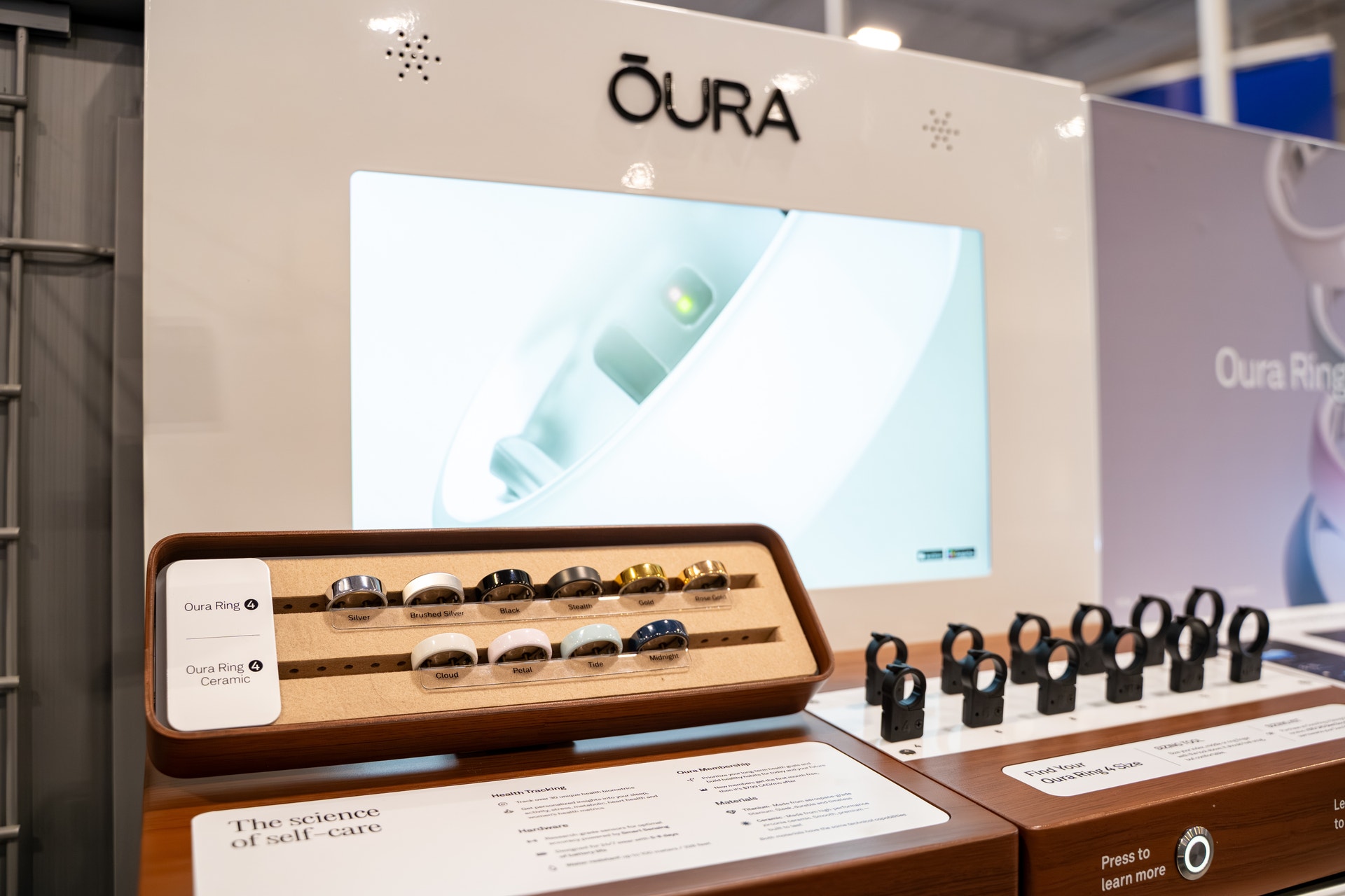 Utställningsdisplay för Oura smarta ringar med en skärm, träbricka med ringmodeller och informationsmaterial.