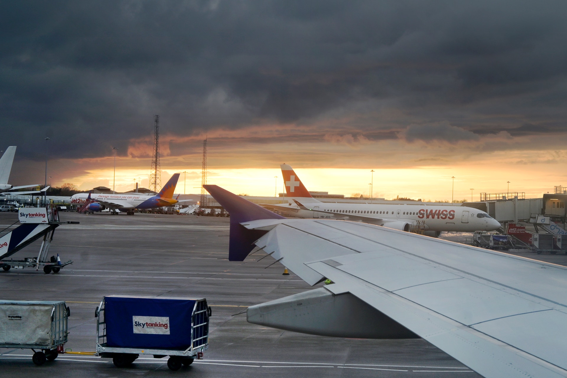 Flygplan parkerade vid flygplatsen under solnedgång med markfordon och servicefordon i förgrunden.