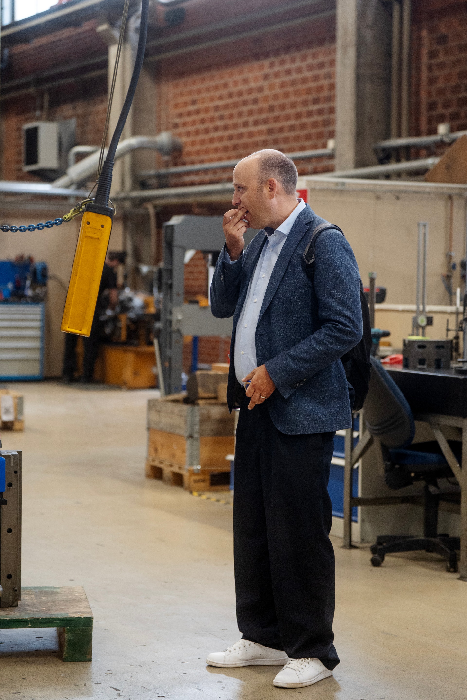 Man i marinblå kavaj står i en industriell fabriksmiljö och ser fundersam ut.