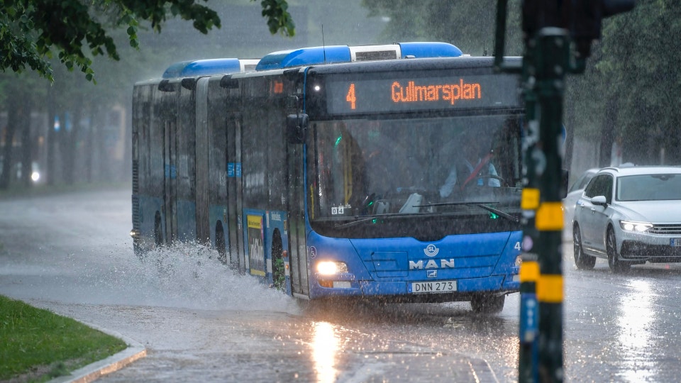 Blå och svart buss kör genom kraftigt regn på en våt gata